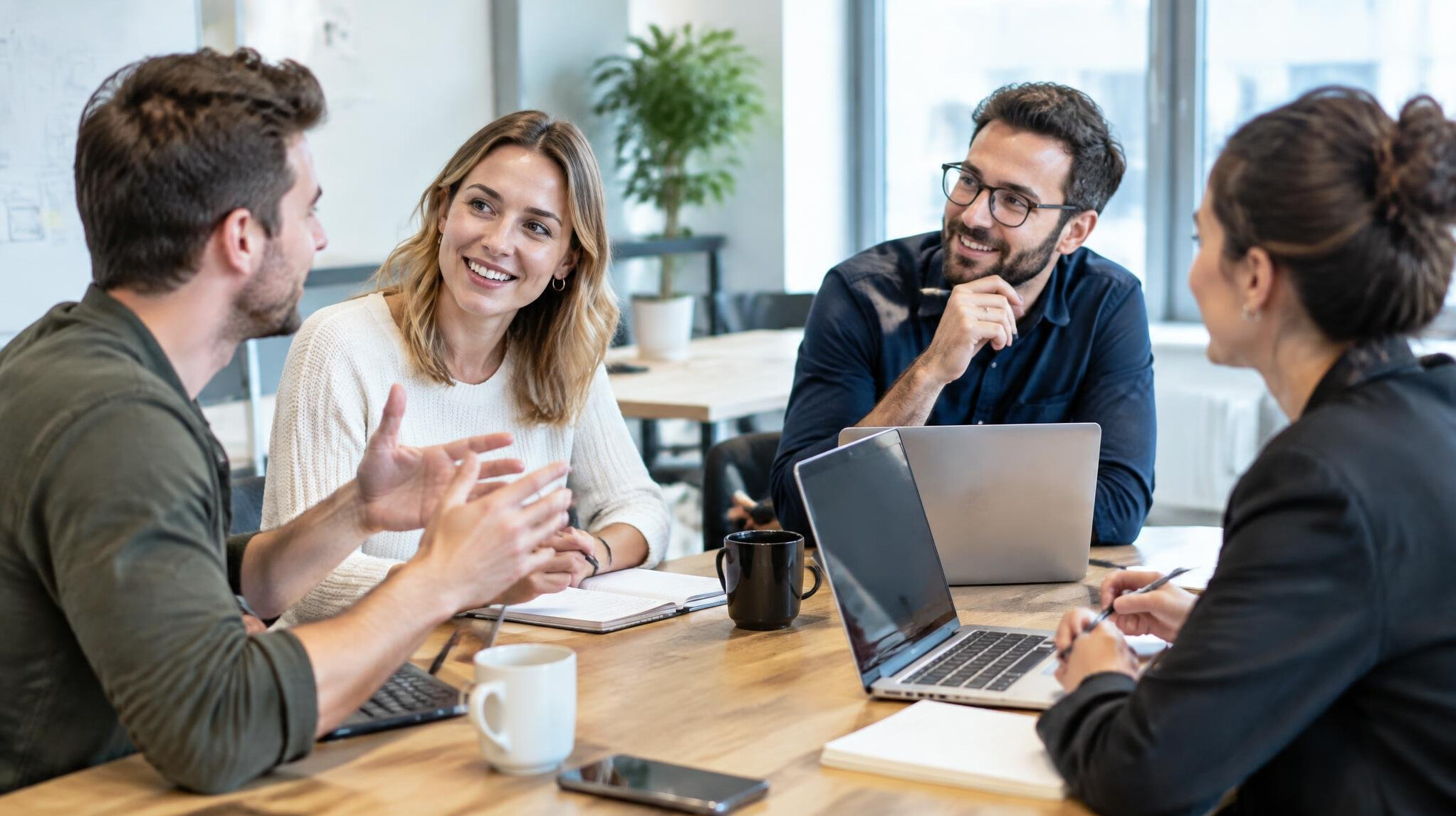Group of colleagues discussing around a table with laptops