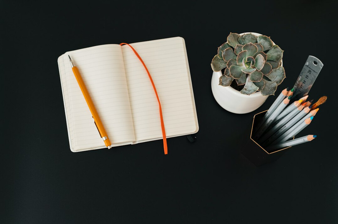 Overhead view of a desk with notebook, pen and laptop